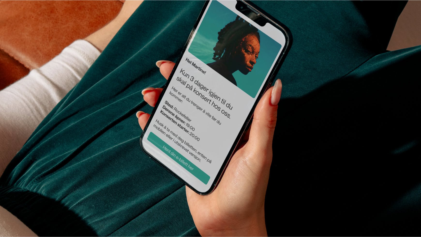 En person holder en mobiltelefon med en digital konsertbillett på skjermen, som viser konsertsted, tid og billettinformasjon.